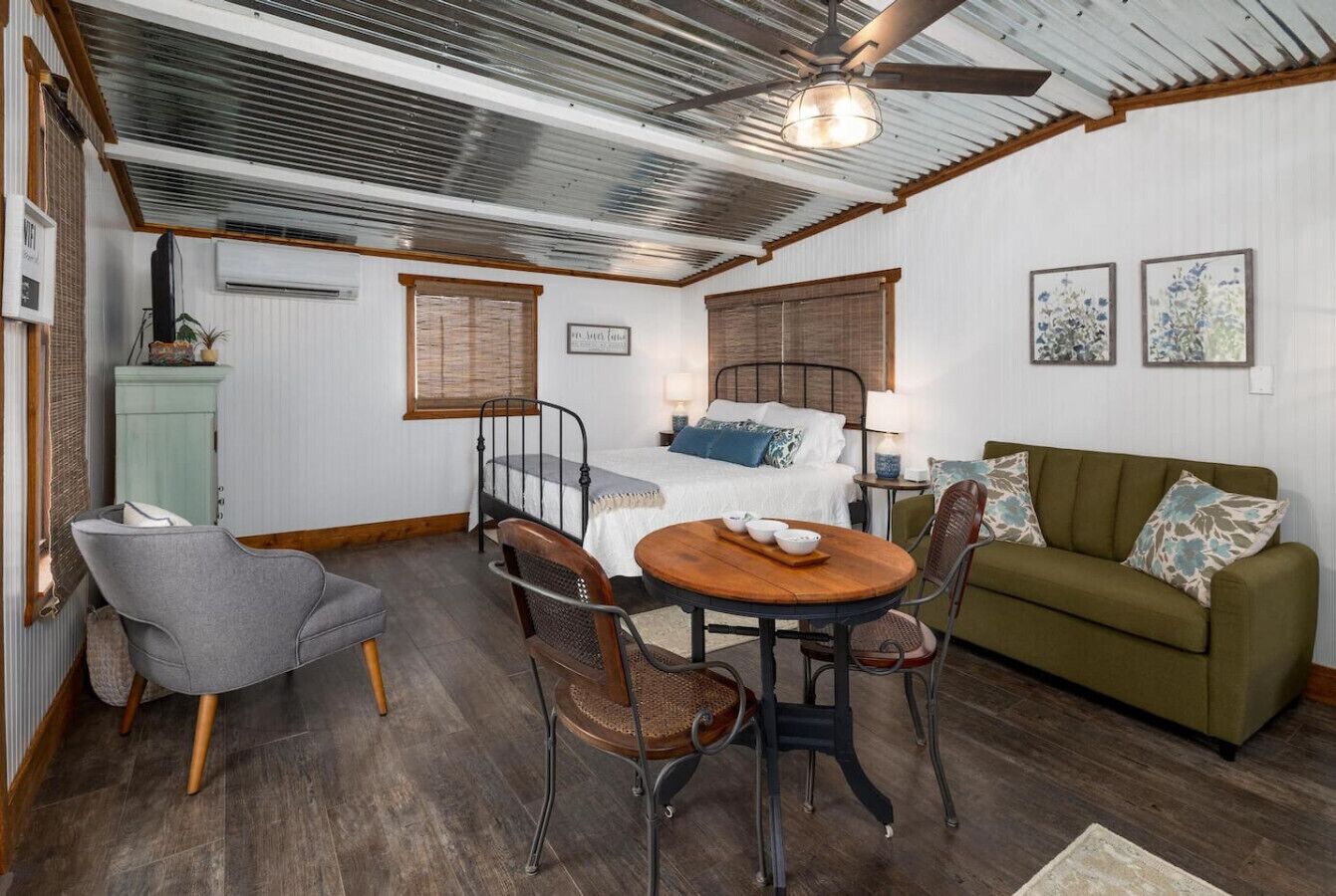 Una habitación acogedora con una cama, un sofá verde, una mesa de comedor con sillas y un pequeño armario.