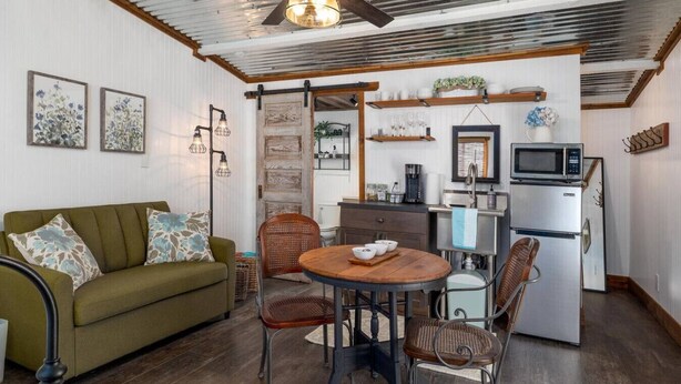 A cozy living room with a sofa, a dining table with chairs, a kitchen area with a refrigerator, and a microwave. - Welcome to the Ladybug Walk DT and Blanco River (Wimberley)