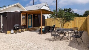 A small cabin with a covered porch, outdoor seating, and a gravel ground. - Welcome to the Ladybug Walk DT and Blanco River (Wimberley)