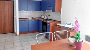 Une cuisine de taille réduite avec des meubles bleus, un plan de travail en bois, un évier et une cuisinière. On y trouve une table à manger avec des chaises et un vase rempli de fleurs.
