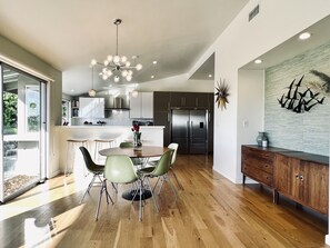 A modern kitchen with a central island, stainless steel appliances, and a dining area with a round table and chairs. - Mid Century View Home in Calabasas (Calabasas)
