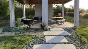 Un patio esterno coperto con tavolo e sedie, immerso in un giardino con un vialetto in pietra.