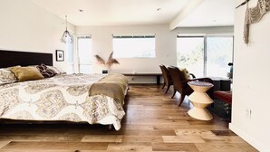 Una camera da letto moderna con un letto grande, pavimento in legno e ampie finestre che lasciano entrare molta luce naturale.
