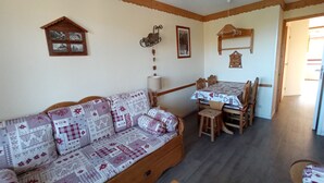 A cozy living room with a wooden sofa, a dining table with chairs, and a small wooden cabinet. - MOUNTAIN-STYLE APARTMENT AT THE FOOT OF THE SLOPES SLEEPS 5 (La plagne - Belle-plagne)