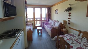 A cozy room with a sofa, a table, and a kitchen area including a stove. - MOUNTAIN-STYLE APARTMENT AT THE FOOT OF THE SLOPES SLEEPS 5 (La plagne - Belle-plagne)