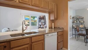 A kitchen with wooden cabinets, a dishwasher, and a window with a view of a pool. - Boutique Stay: Near Beach,  PSP4, Billiard or PingPong, Fire Pit, Private Yard (New Port Richey)