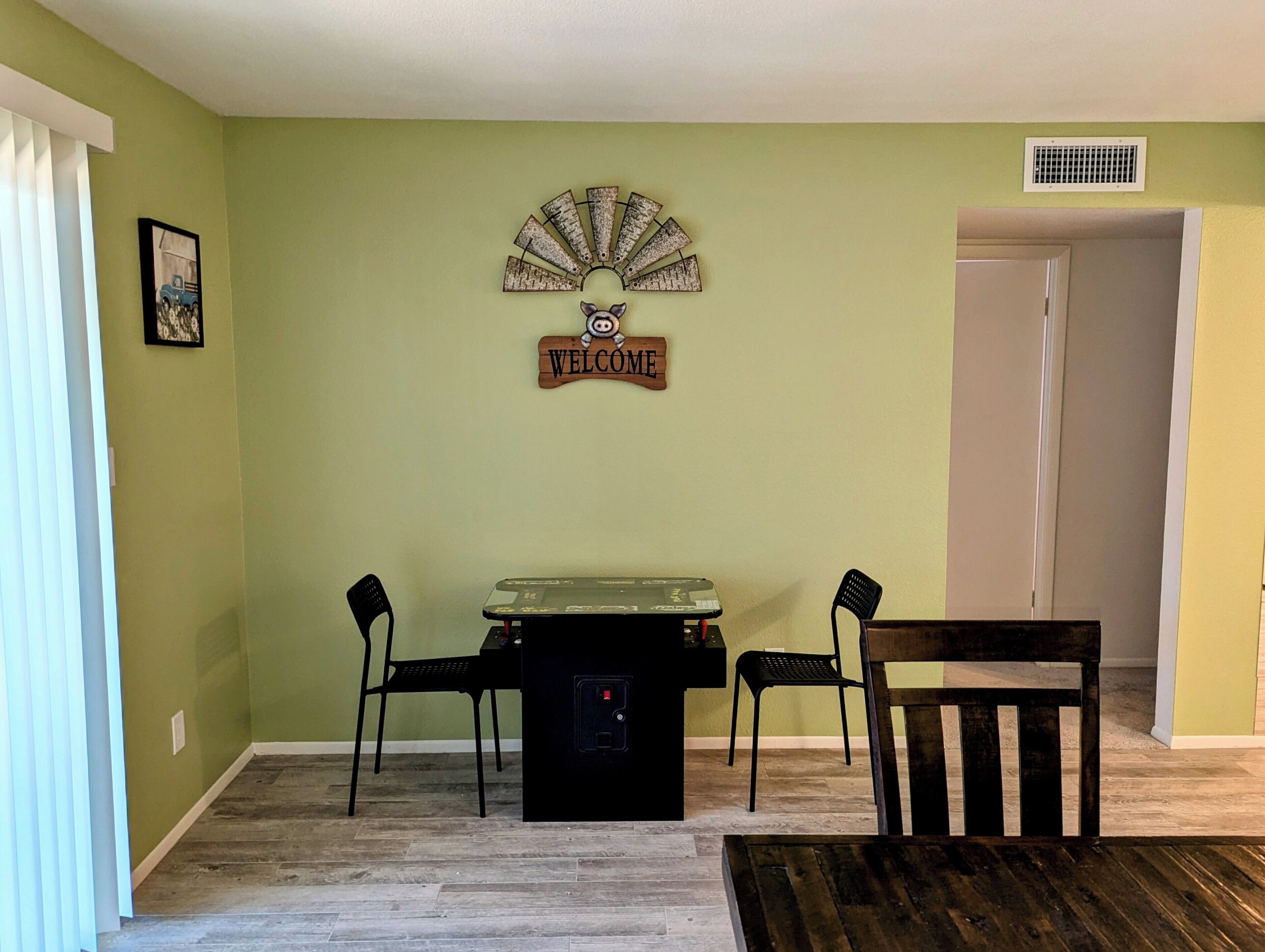 A room with a green wall, a welcome sign, a small table with chairs, and a door.