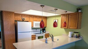 A kitchen with wooden cabinets, a white refrigerator, a microwave, an oven, a sink, and a granite countertop.