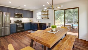 Une cuisine moderne dotée d’appareils électroménagers en acier inoxydable, d’une table à manger en bois et d’une grande porte-fenêtre coulissante donnant sur un patio extérieur.