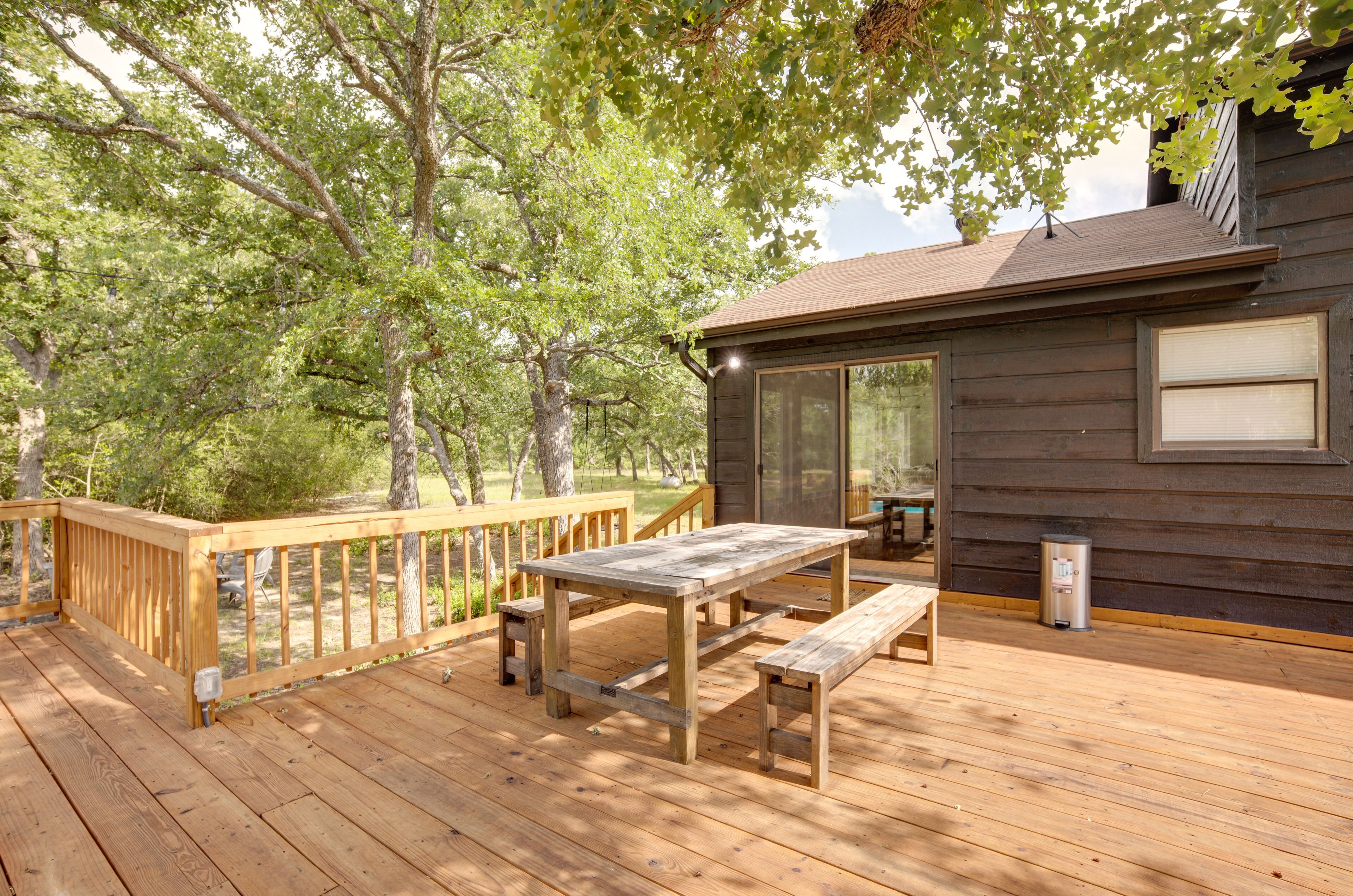 A wooden deck with a picnic table and benches, surrounded by trees.