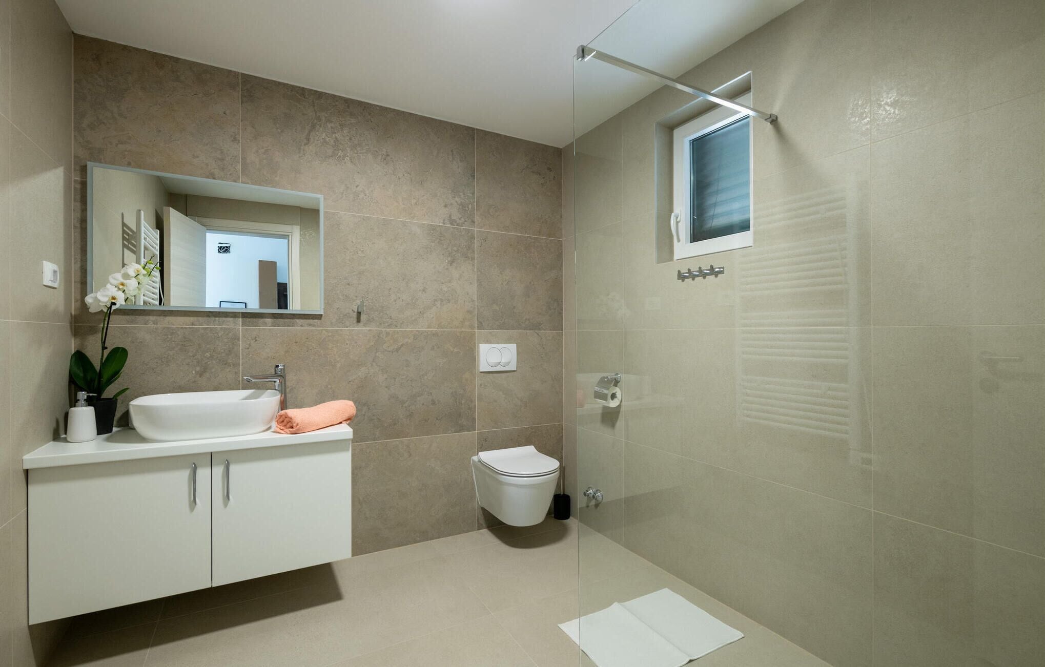 A modern bathroom with a white vanity, a glass shower enclosure, and a toilet.