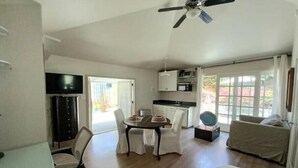 A spacious living area with a dining table, chairs, a sofa, a ceiling fan, and a kitchen area with cabinets and a microwave.