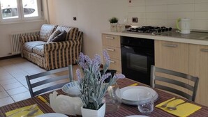Un comedor con una mesa dispuesta para cuatro personas, un sofá y una cocina al fondo.