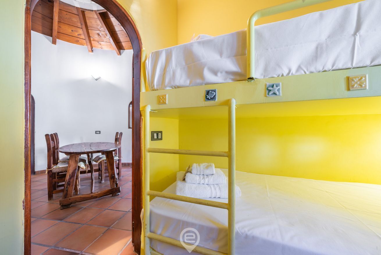 A bunk bed room with a wooden table and chairs, a tiled floor, and a small window.