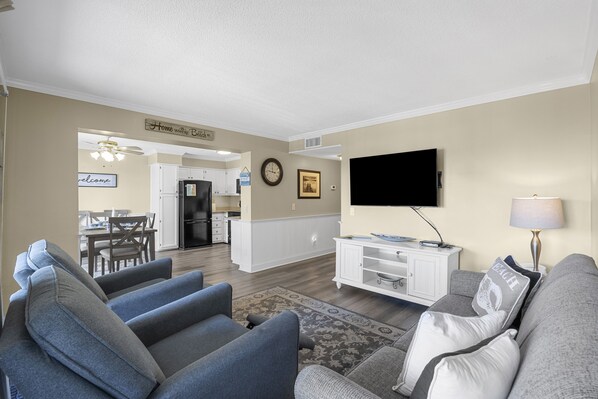 Una sala de estar con televisión, sofá y un comedor al fondo.