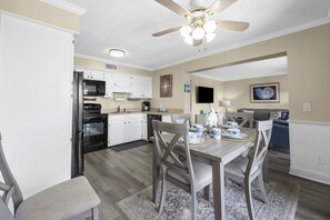 Una cocina moderna con armarios blancos, un refrigerador negro y un comedor con una mesa y sillas de madera.