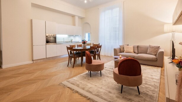 A modern living room with a sofa, chairs, a dining table, and a kitchen in the background. - Apartments Florence - Buontalenti Exclusive (Firenze)
