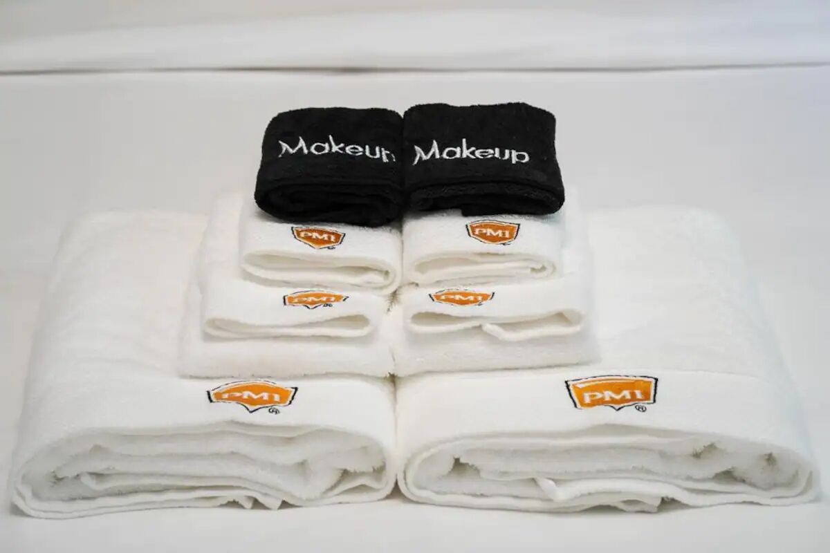 A neatly folded white towel with a PMI logo and the word "Makeup" on a black towel placed on top.