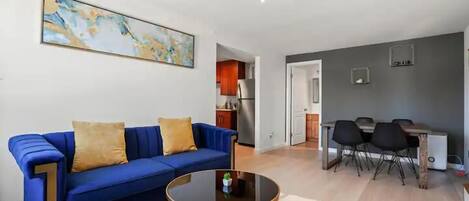 Un salon avec un canapé bleu, une table basse ronde et un tableau accroché au mur.