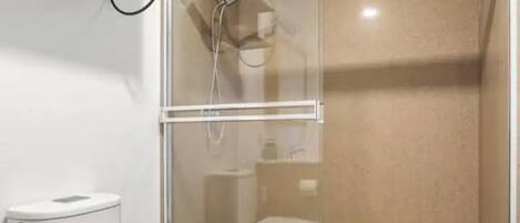 Ein Badezimmer mit Toilette, einer Duschkabine und einem Regal über der Toilette.