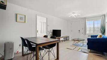 Una sala de estar moderna con comedor, un sofá azul y una televisión.