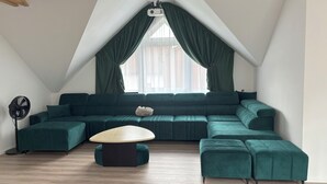 Uma sala de estar moderna com um sofá seccional grande, uma mesa de centro redonda e um ventilador.