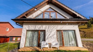 Uma casa moderna com telhado inclinado, janelas grandes e um deck de madeira com duas cadeiras.