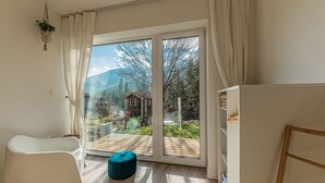 Quarto moderno com uma grande porta de vidro deslizante que dá para um deck externo, uma cadeira branca e um banquinho azul.