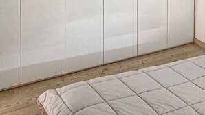 A bedroom with a large wardrobe, a bed with a quilted cover, and a wooden floor.