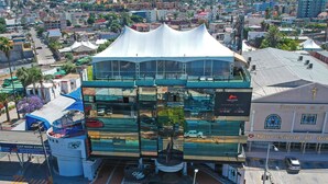 A multi-story building with a modern glass facade and a distinctive white roof. - Hotel Sunio City (Tijuana)
