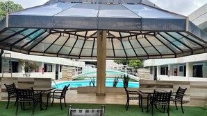 A poolside area with a covered seating area, artificial grass, and a pool with a bridge. - Hotel Sunio City (Tijuana)