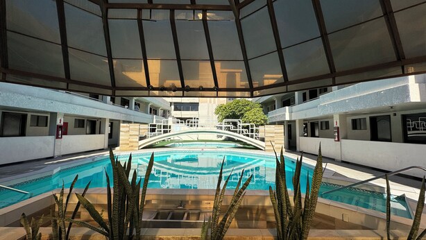 An indoor swimming pool with a glass bridge, surrounded by plants and a modern architectural design. - Hotel Sunio City (Tijuana)