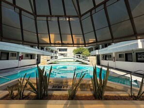Une piscine intérieure dotée d’un pont de verre, entourée de plantes et présentant un design architectural moderne.