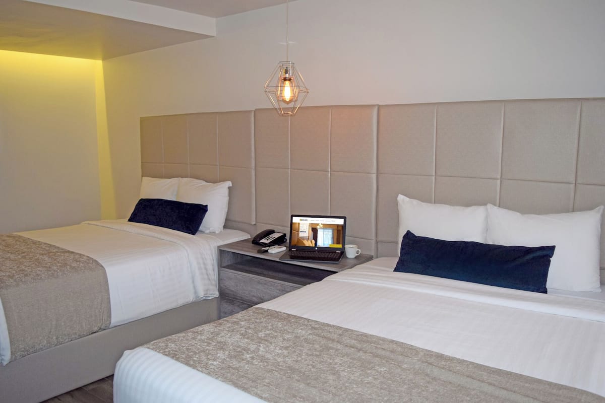 A hotel room with two beds, a laptop on the nightstand, and a hanging light fixture.