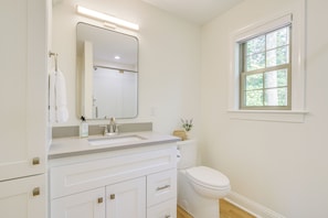 A bathroom with a white vanity, a mirror, a toilet, and a window.