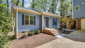 A two-story house with a front porch, a brick foundation, and a small front yard with mulch and plants. - Beautiful Raleigh Cottage Rental: 5 Mi to Downtown (Raleigh)