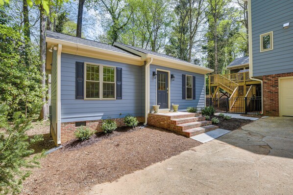 A two-story house with a front porch, a brick foundation, and a small front yard with mulch and plants.