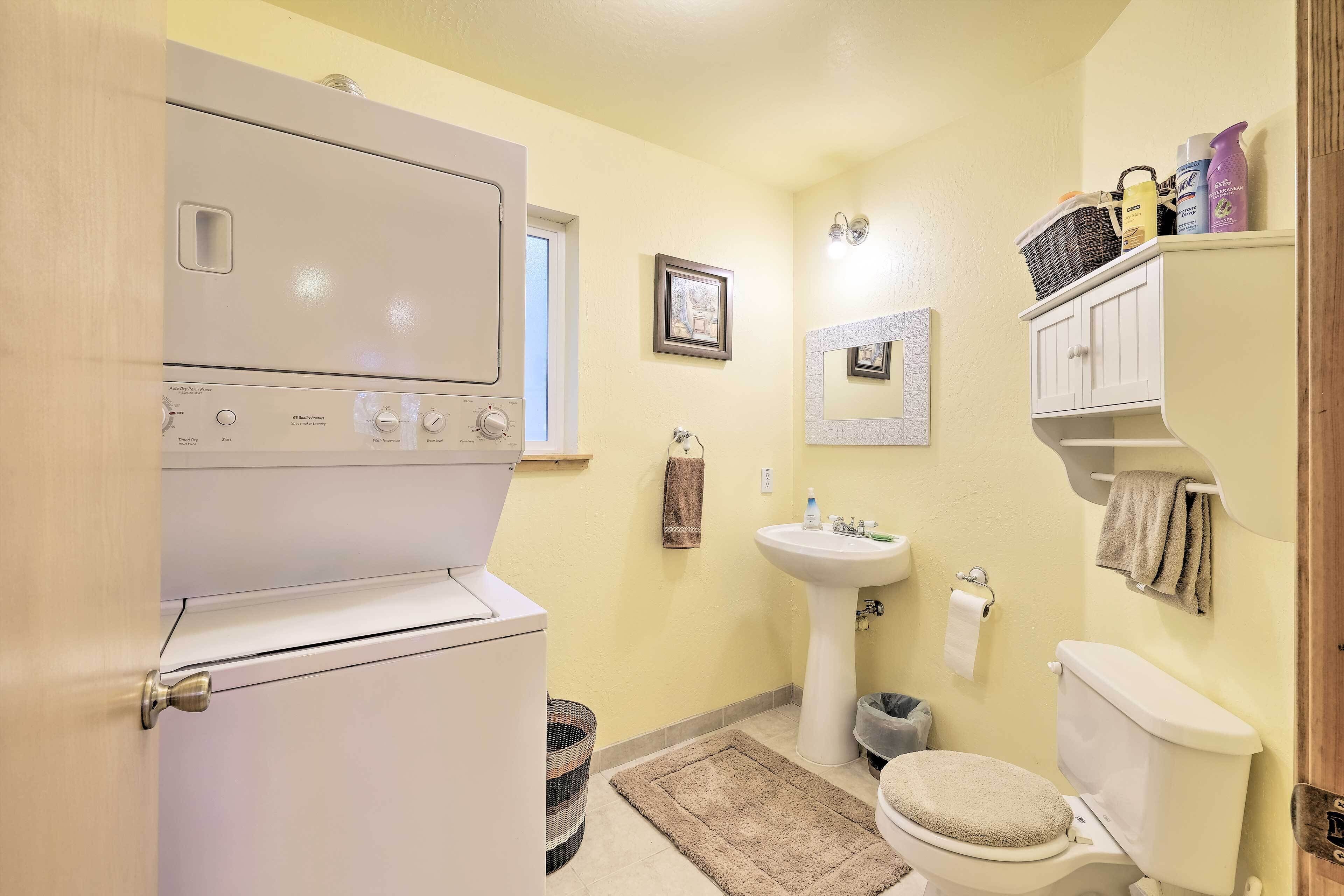 Un baño pequeño con inodoro blanco, lavamanos, espejo, una ventana pequeña y una lavadora.