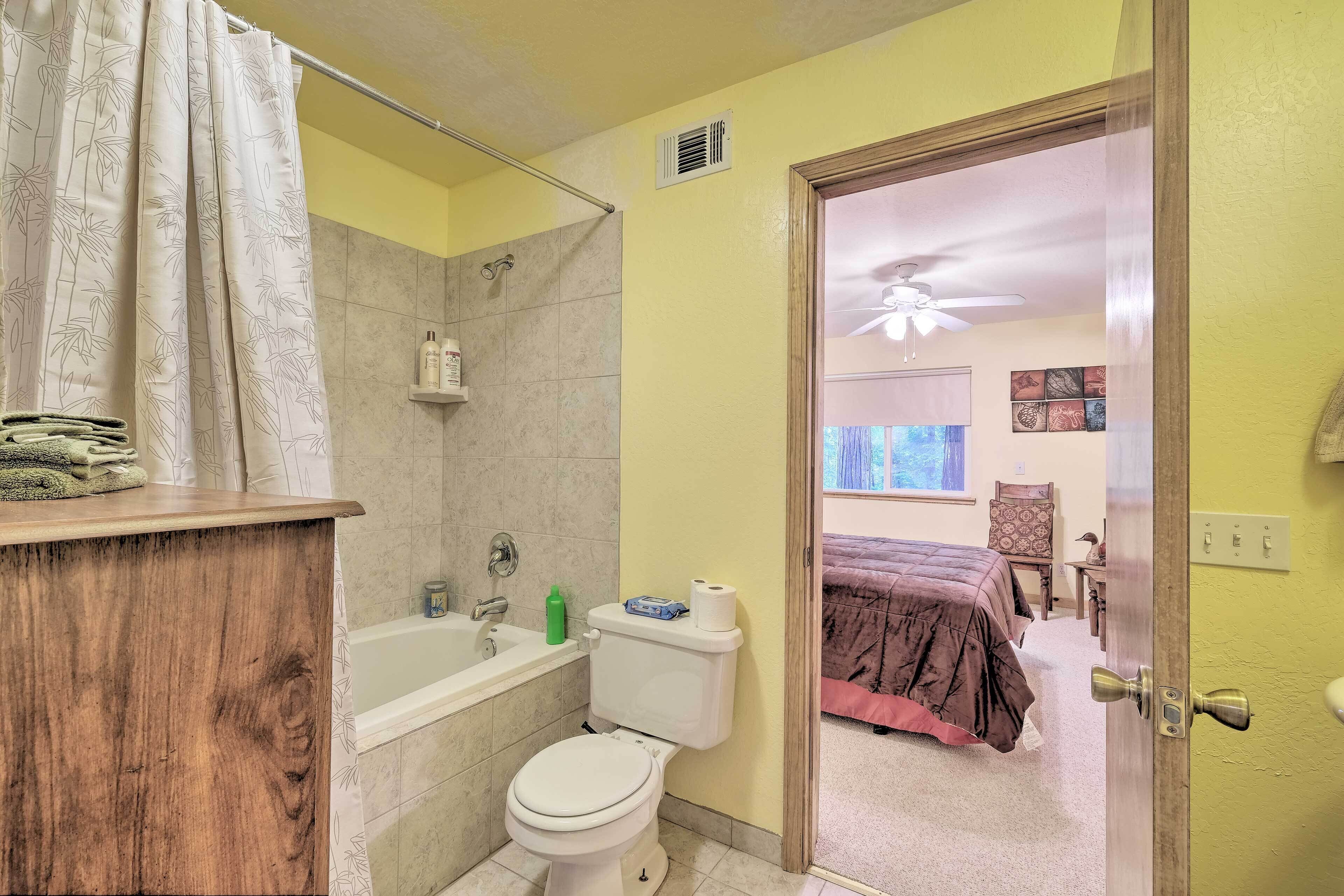 A bathroom with a toilet, bathtub, and shower. A wooden counter and a towel rack are visible.