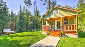 A small cabin with a porch, a deck, and a hot tub in a forested area. - Rustic-chic Woodland Hideaway w/ Hot Tub! (Sandpoint)