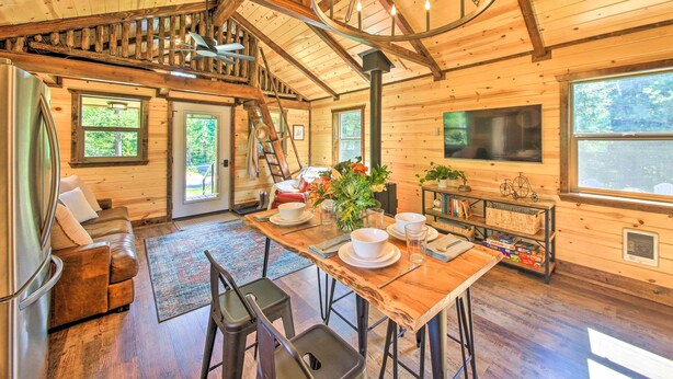 A spacious cabin with a wooden interior, a dining area with a large table, and a staircase leading to an upper level. - Rustic-chic Woodland Hideaway w/ Hot Tub! (Sandpoint)