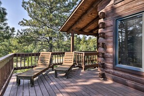 A wooden deck with two lounge chairs and a table, overlooking a forested area.