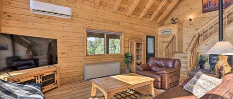 Acogedor interior de cabaña de madera con techo de madera, chimenea, mobiliario de cuero y una escalera que conduce a un nivel superior.