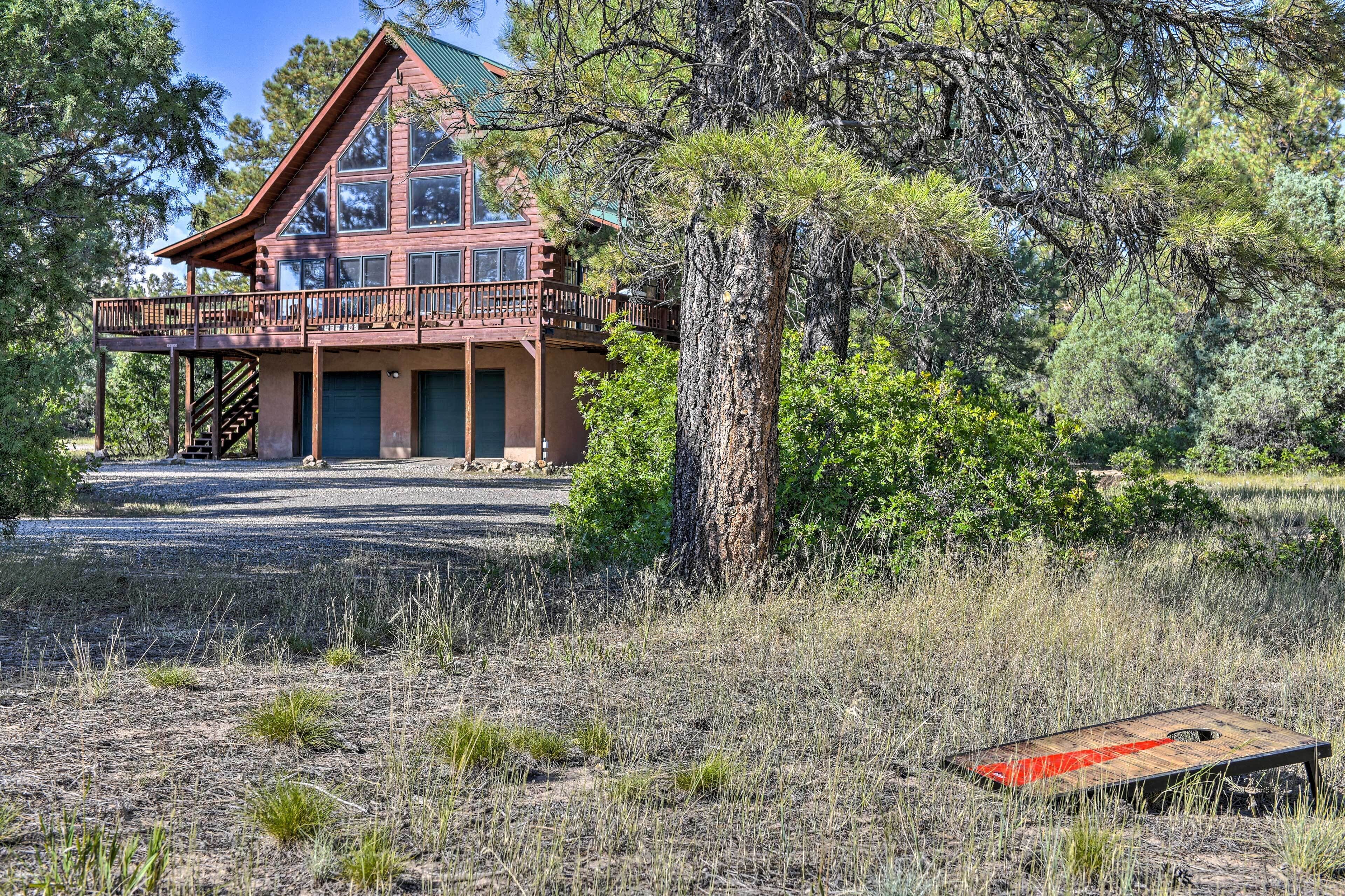A large, multi-story cabin with a balcony, surrounded by trees and a gravel driveway.