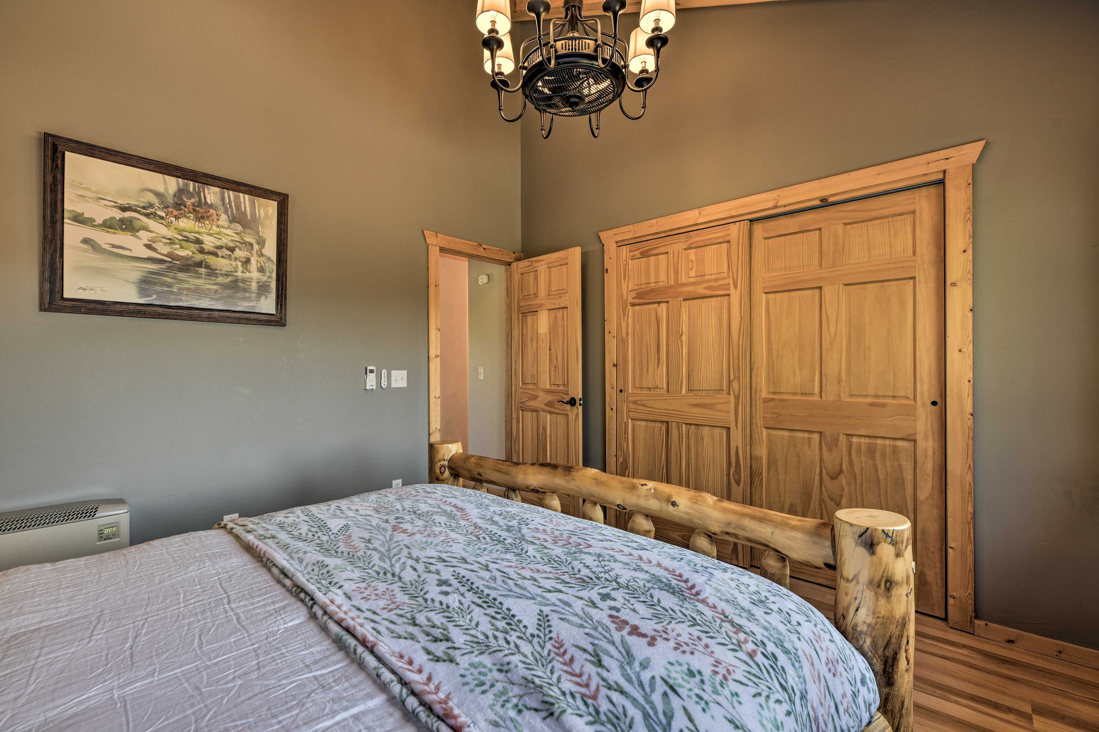 A bedroom with a bed, a wooden wardrobe, a painting on the wall, and a ceiling light fixture.