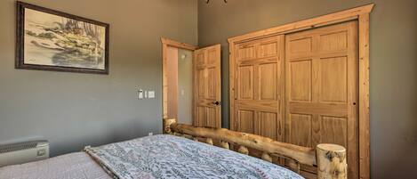 A bedroom with a bed, a wooden wardrobe, a painting on the wall, and a ceiling light fixture.