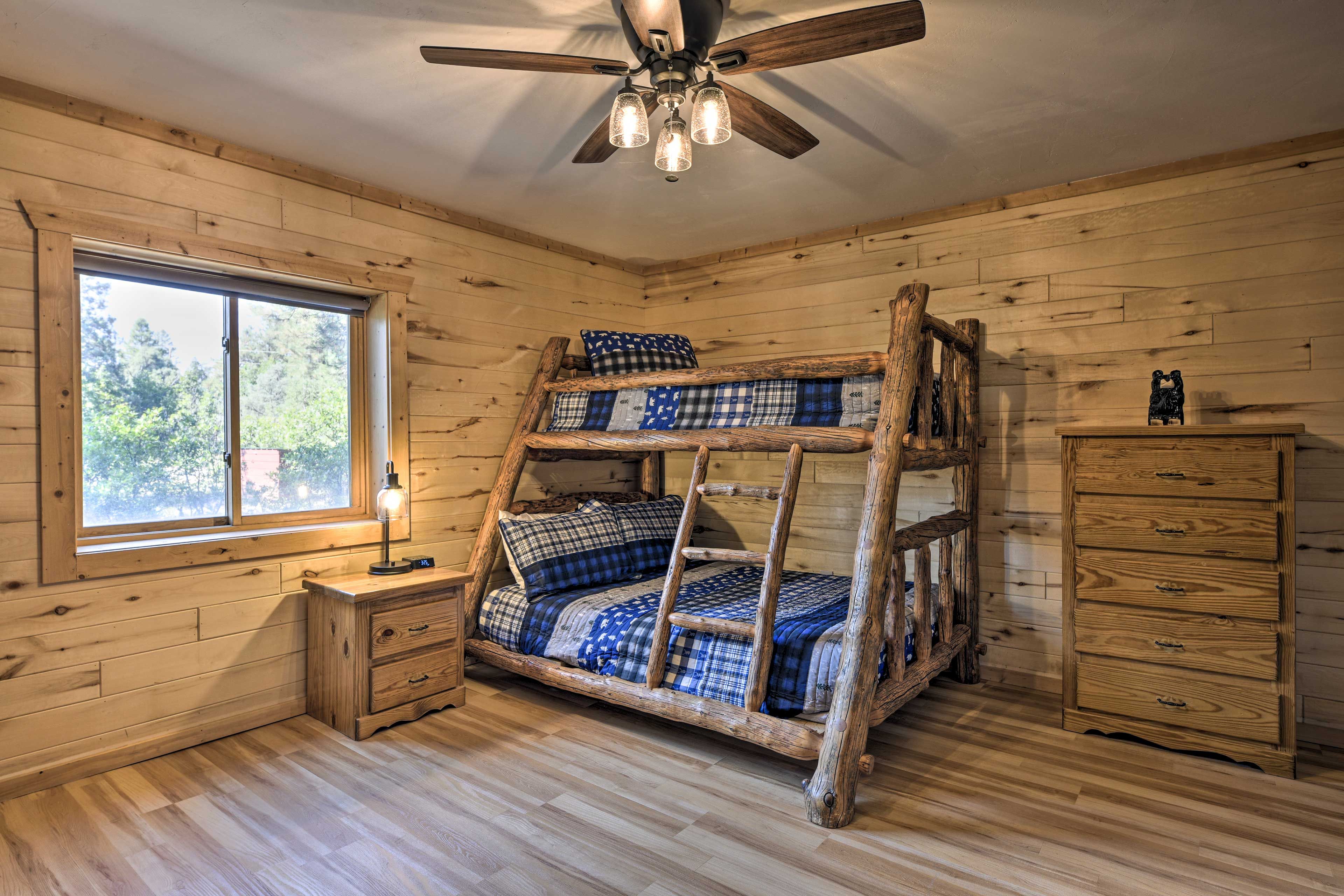 A rustic wooden room with a bunk bed, a wooden dresser, and a window with a view of trees.