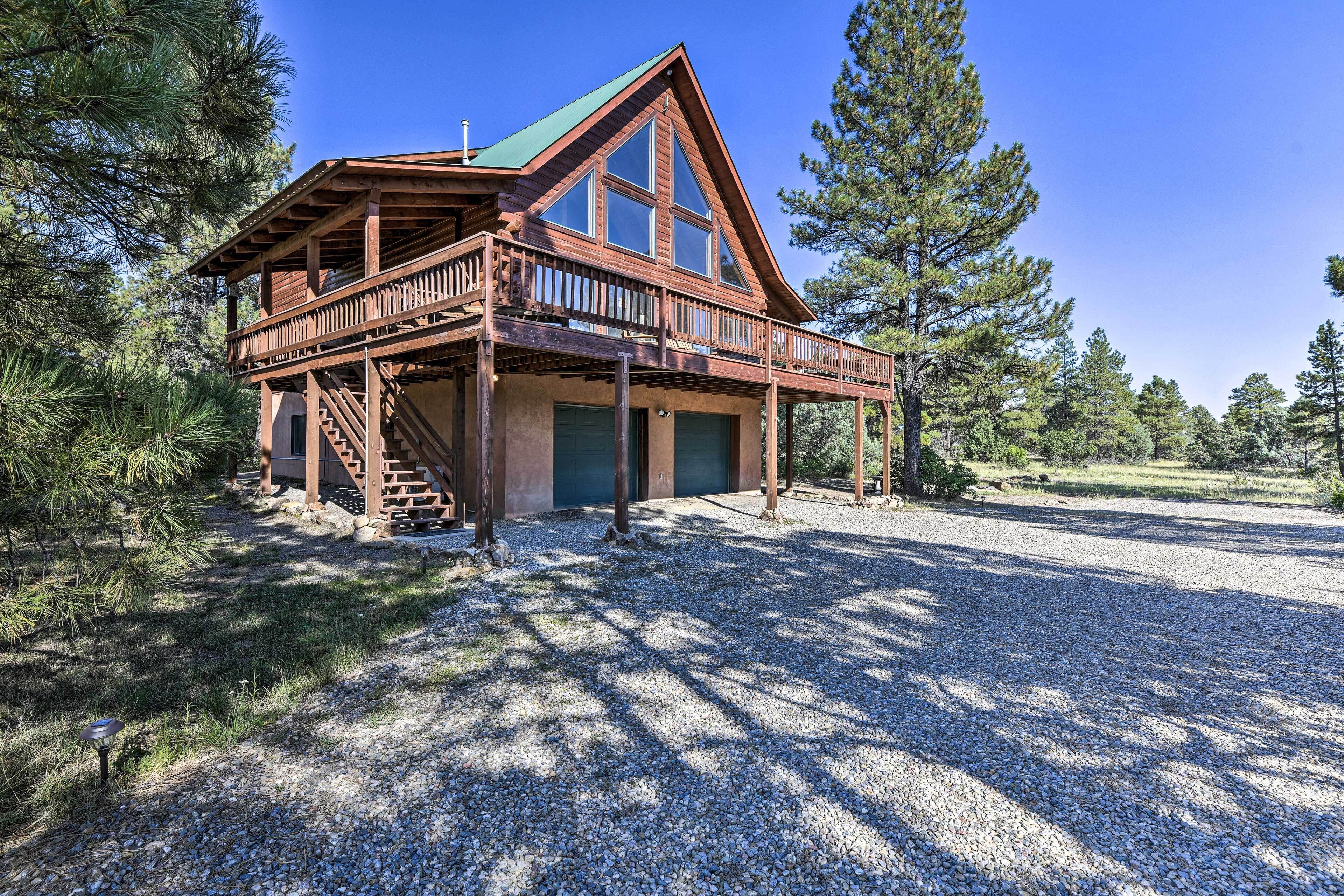 A two-story wooden cabin with a balcony, surrounded by trees.