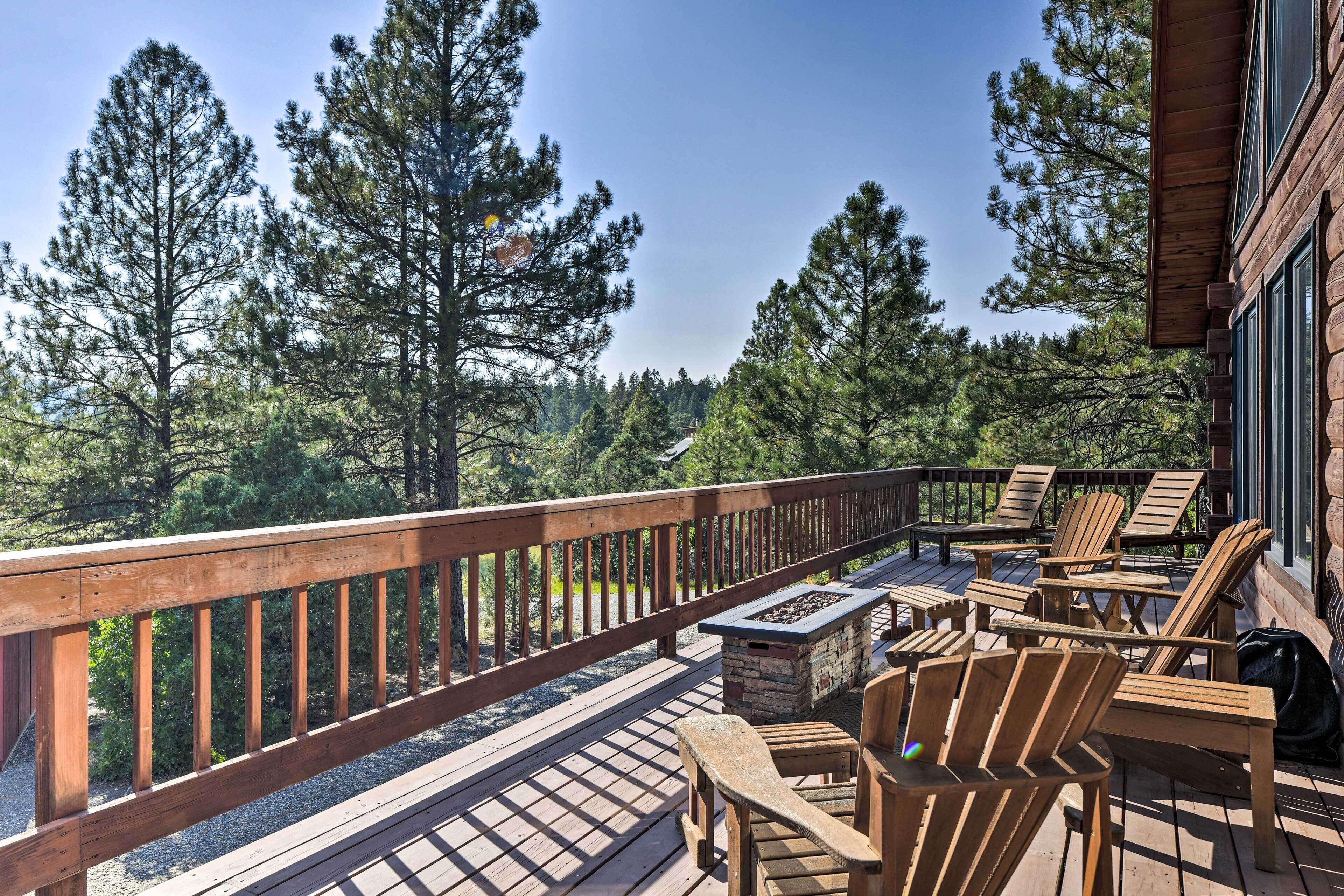 Une terrasse en bois avec des fauteuils Adirondack et une cheminée en pierre, donnant sur une zone boisée.