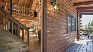 A wooden cabin interior with a staircase leading to a loft bedroom, a dining area, and a porch with a view of the outdoors. - Lazy Beaver Lodge Pagosa Cabin w/ Deck, Fire Pit (Pagosa Springs)